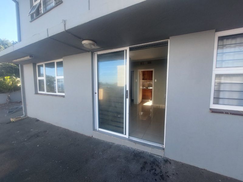 Rear exterior view of the apartment featuring a sliding glass door entrance, aluminium window frames, and paved outdoor area.