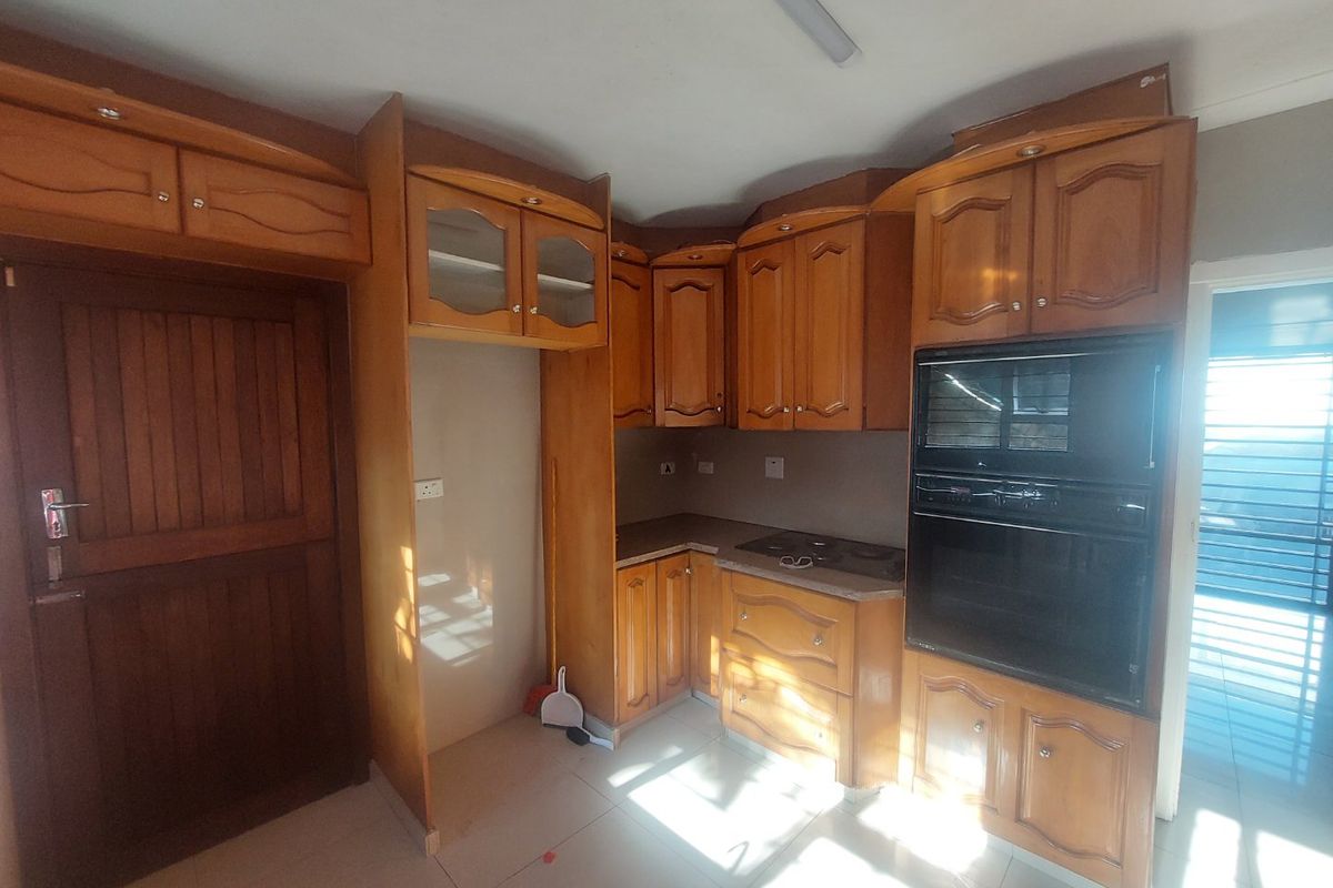 A functional kitchen featuring built-in wooden cabinetry, an integrated oven and hob, and tiled flooring, offering a classic layout ready for modernization.