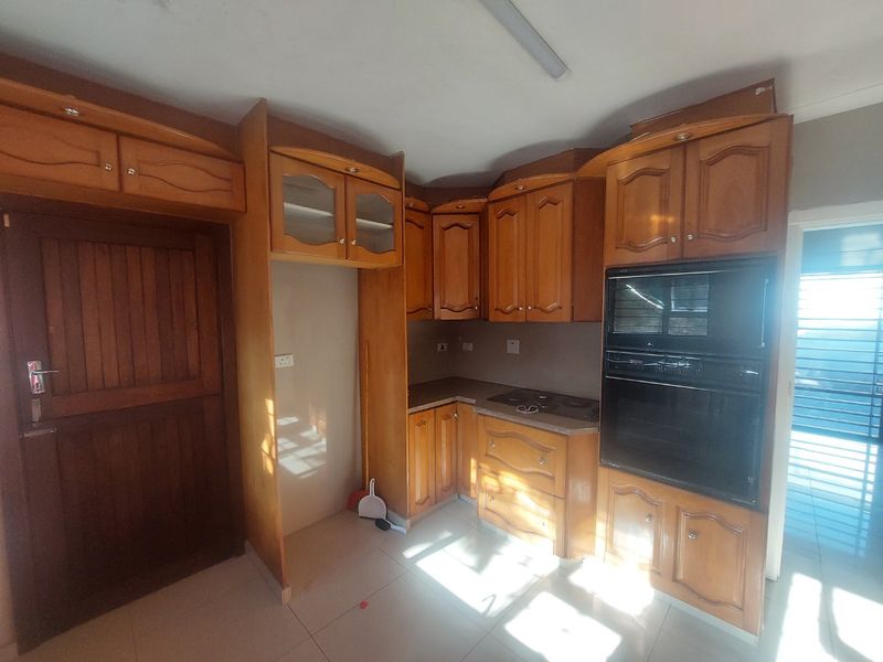 A functional kitchen featuring built-in wooden cabinetry, an integrated oven and hob, and tiled flooring, offering a classic layout ready for modernization.