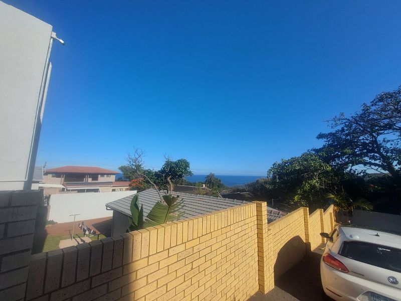 An elevated view overlooking neighboring properties with a distant ocean horizon visible under a clear blue sky.
