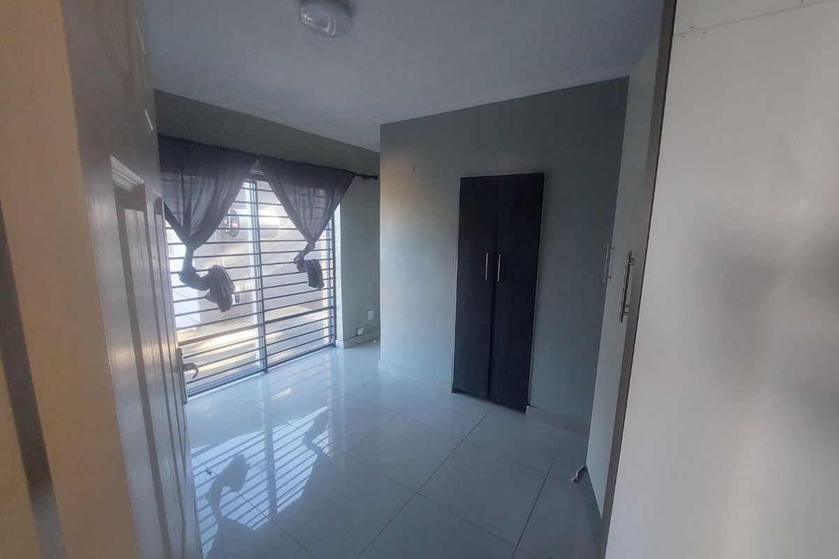 A bright, empty bedroom featuring tiled flooring, a built-in wardrobe, and a sliding door with security bars leading to the exterior.