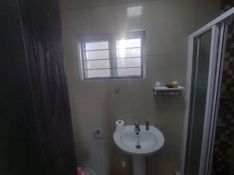 A functional bathroom featuring a pedestal basin, mixer tap, and a shower enclosure with tiled wall finishes.