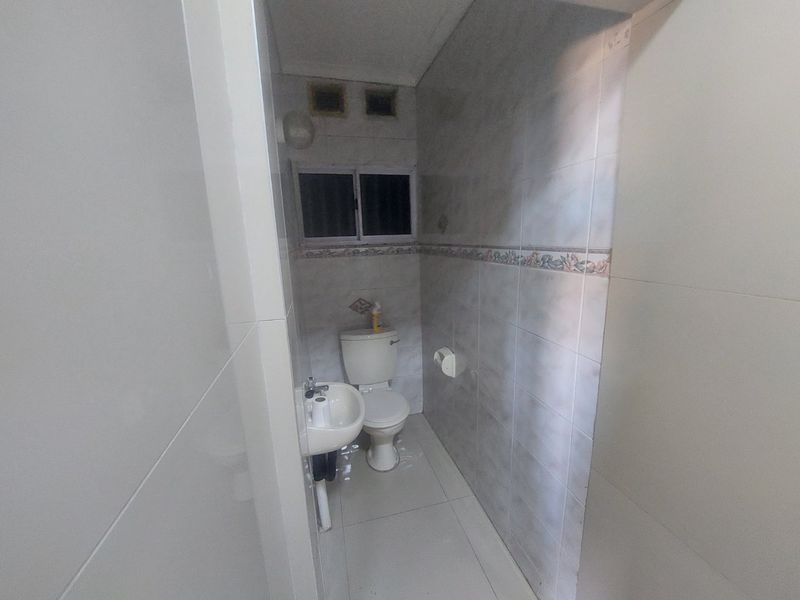 A compact bathroom featuring tiled walls and floors, equipped with a standard toilet and pedestal basin, requiring cosmetic updates to improve its overall condition.