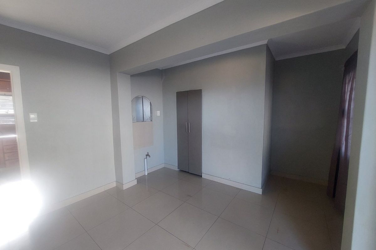 An empty living area featuring neutral tiled flooring, a built-in cupboard, and a dedicated plumbing connection point.