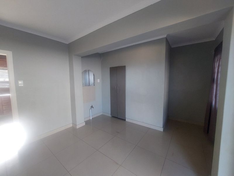 An empty living area featuring neutral tiled flooring, a built-in cupboard, and a dedicated plumbing connection point.