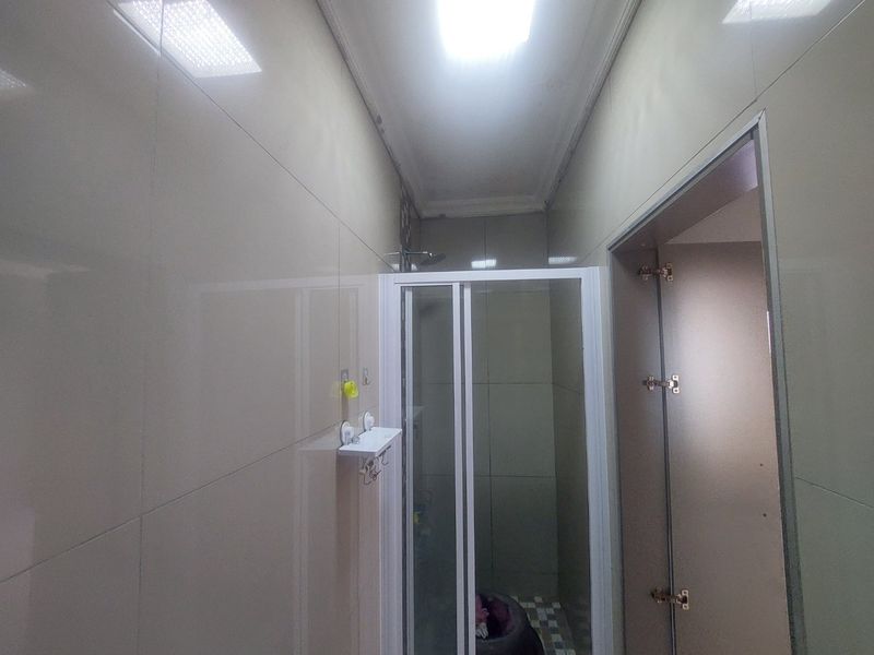 A compact bathroom featuring a shower enclosure with tiled walls and recessed ceiling lighting, requiring some maintenance to finishes.