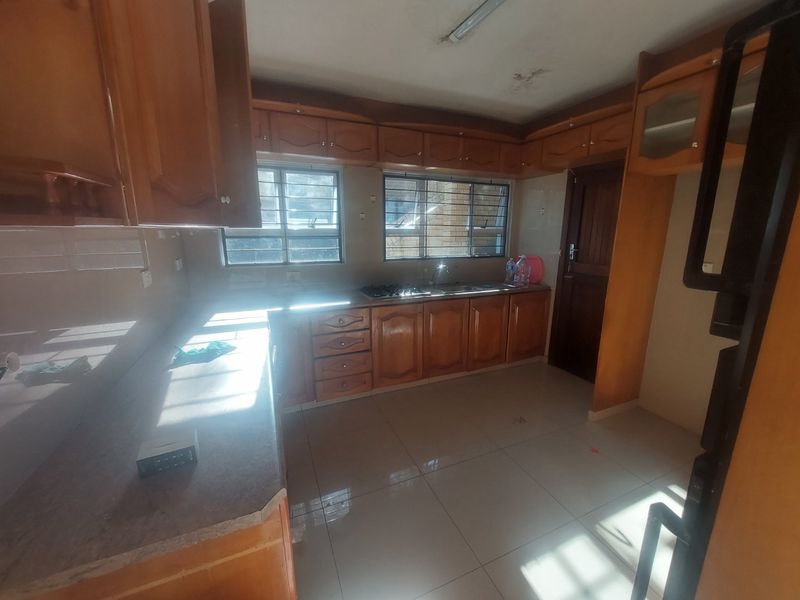 A functional kitchen featuring wooden cabinetry, laminate countertops, a gas hob, and tiled flooring, offering a blank canvas for potential modern updates.