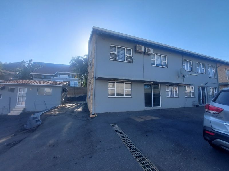 Front exterior view of a multi-story apartment building featuring grey painted walls, aluminium window frames, and an asphalt driveway with drainage.
