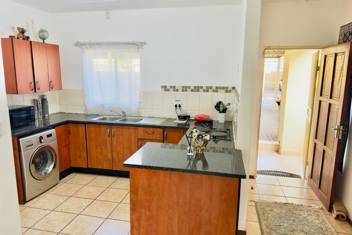 Functional kitchen featuring laminate cabinetry, granite countertops, tiled backsplash, and integrated laundry space, offering a practical layout with direct access to the exterior.