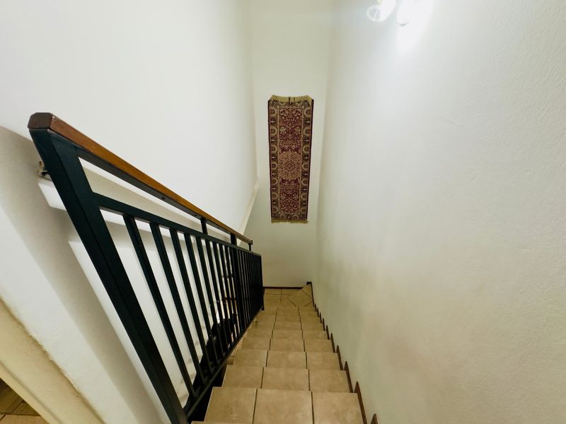 A functional staircase featuring tiled steps, a black metal balustrade, and a wooden handrail, providing access between levels in the apartment.