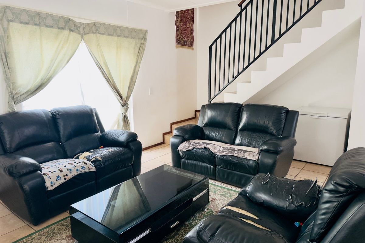 A living room area featuring tiled flooring and a staircase with a black metal balustrade.