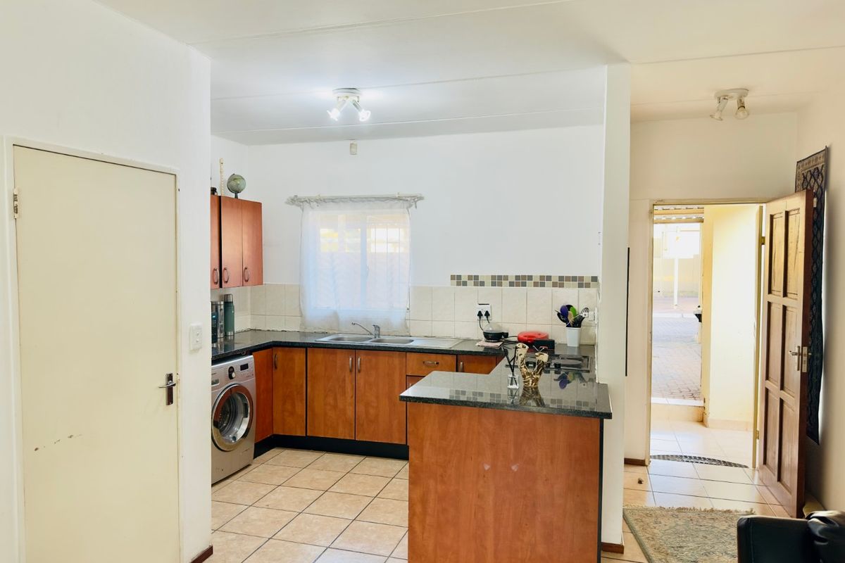 Functional kitchen featuring laminate cabinetry, granite countertops, tiled splashback, and ceramic flooring, with direct access to the exterior entrance.
