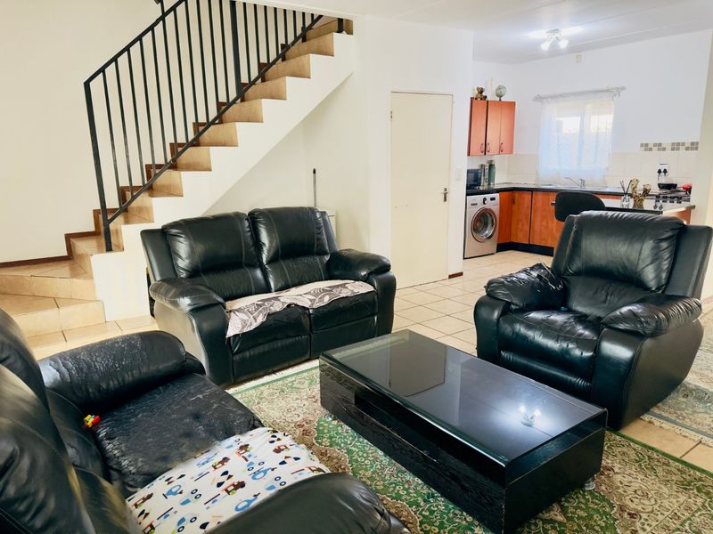 Open-plan living area featuring a staircase with metal balustrade and an adjacent kitchen with built-in cabinetry and tiled flooring throughout.