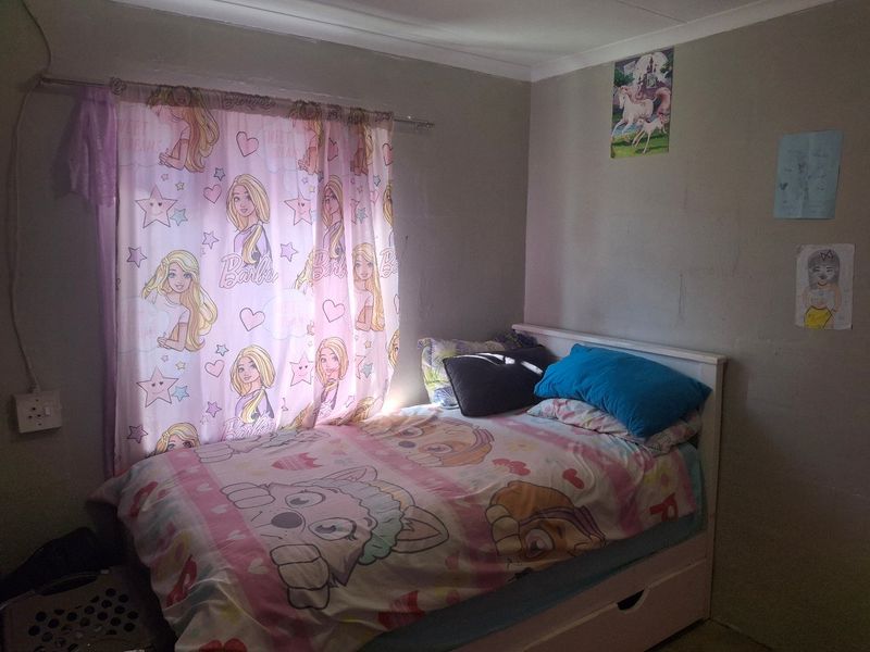 A standard bedroom featuring a window with a curtain rod and wall-mounted electrical outlet.