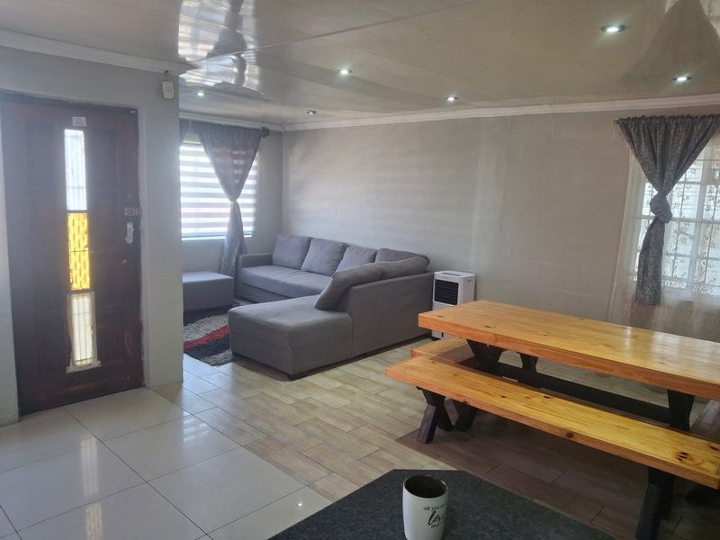 Open plan living and dining area featuring a mix of tiled flooring, recessed downlighting, and a timber entrance door.