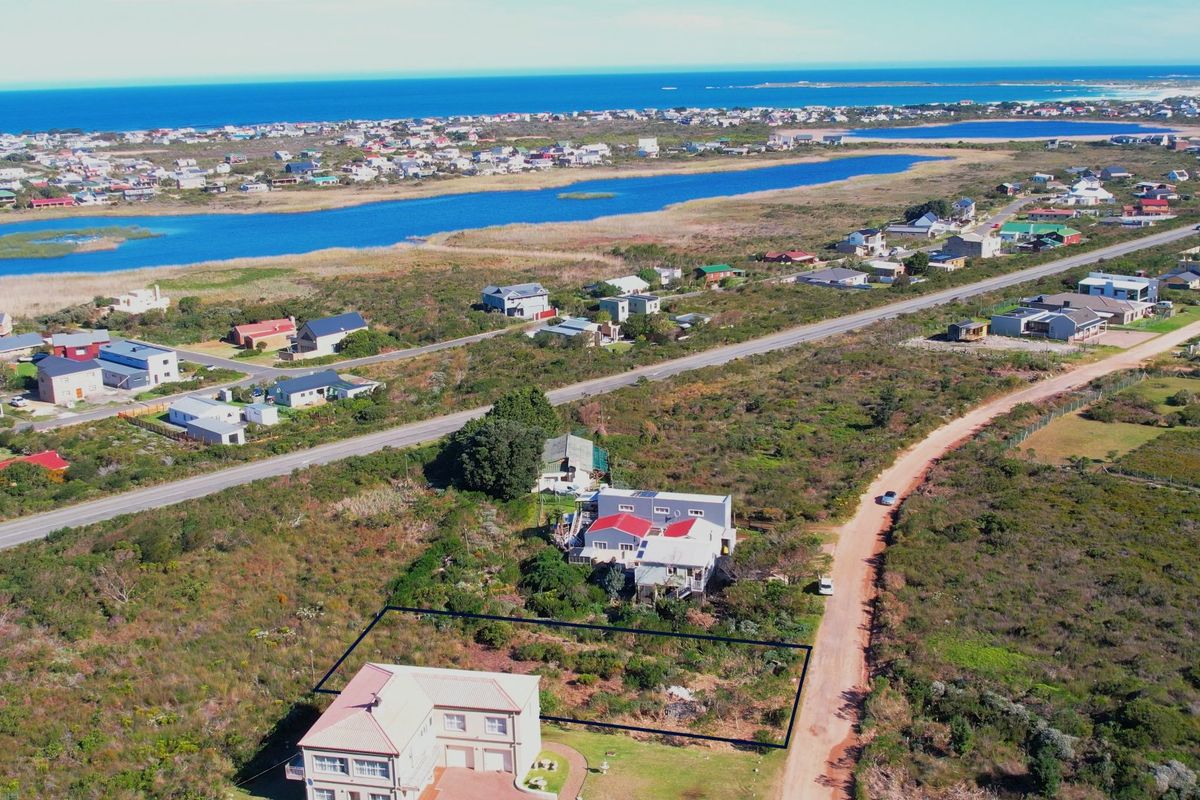 Aerial view of a residential vacant land plot situated in a coastal area with surrounding neighborhood and landscape views.