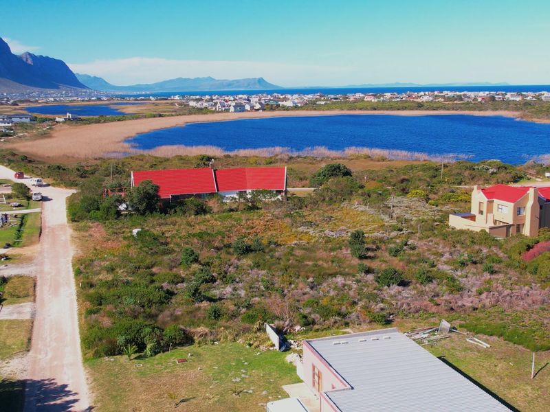 Aerial view of a vacant residential plot featuring natural coastal vegetation, adjacent to a lake and established residential properties.