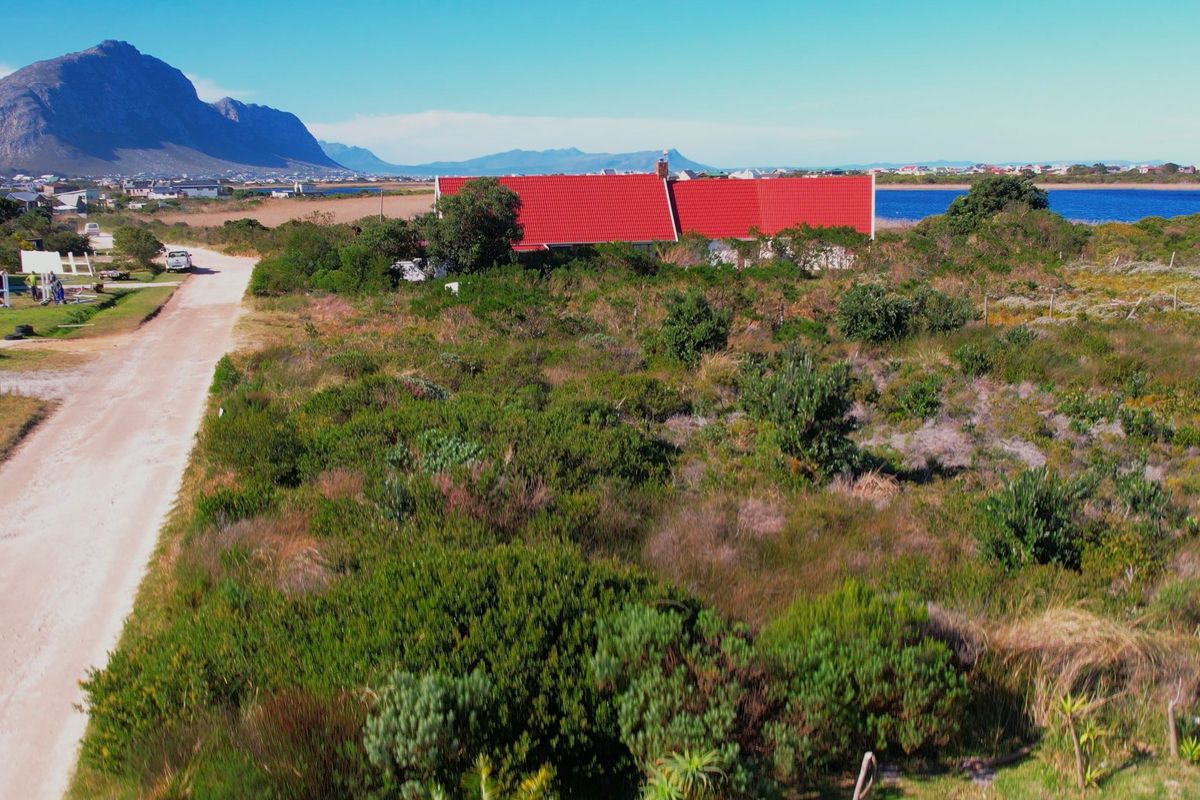 Aerial view of a vacant residential plot featuring natural vegetation and access to a dirt road with distant mountain and water views.