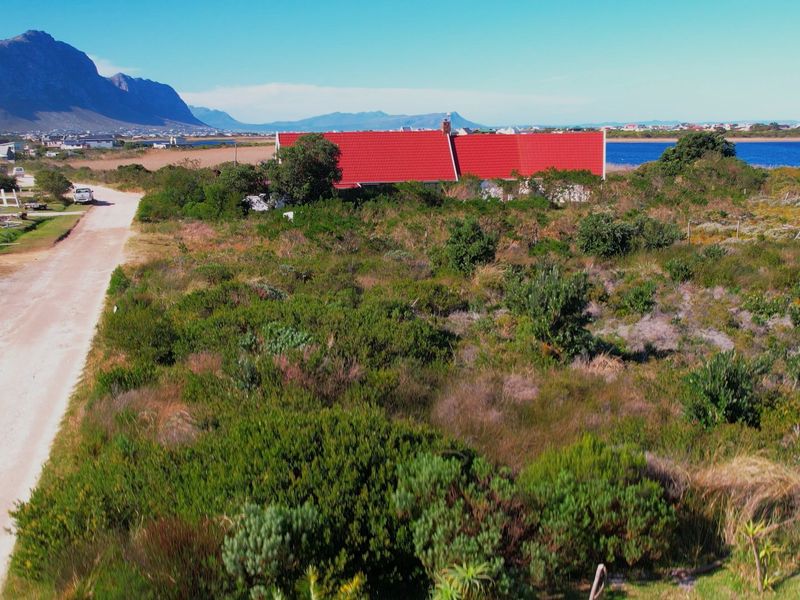 Aerial view of a vacant residential plot featuring natural vegetation and access to a dirt road with distant mountain and water views.