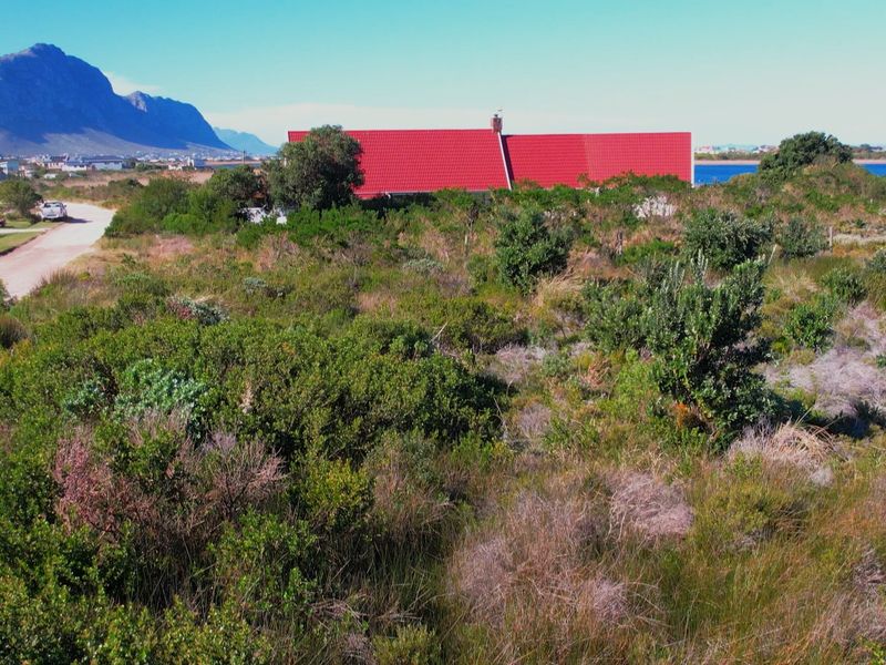 An aerial view of a vacant residential plot featuring natural vegetation, with a distant view of the coastline and surrounding landscape.
