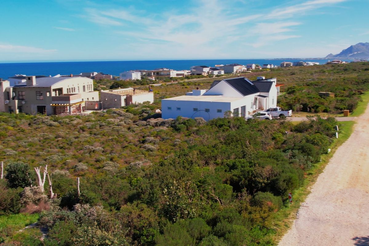 Aerial view of a vacant residential plot in a coastal estate, featuring natural vegetation and proximity to the ocean.