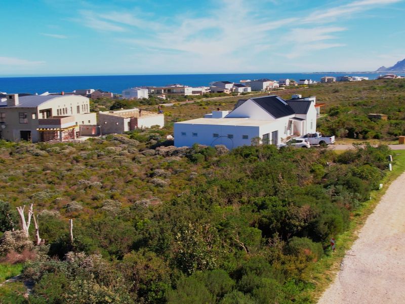 Aerial view of a vacant residential plot in a coastal estate, featuring natural vegetation and proximity to the ocean.