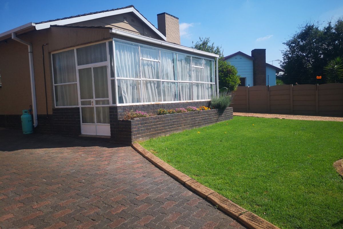 Rear view of the property featuring an enclosed patio, brick planter box, paved driveway, and a well-maintained lawn.