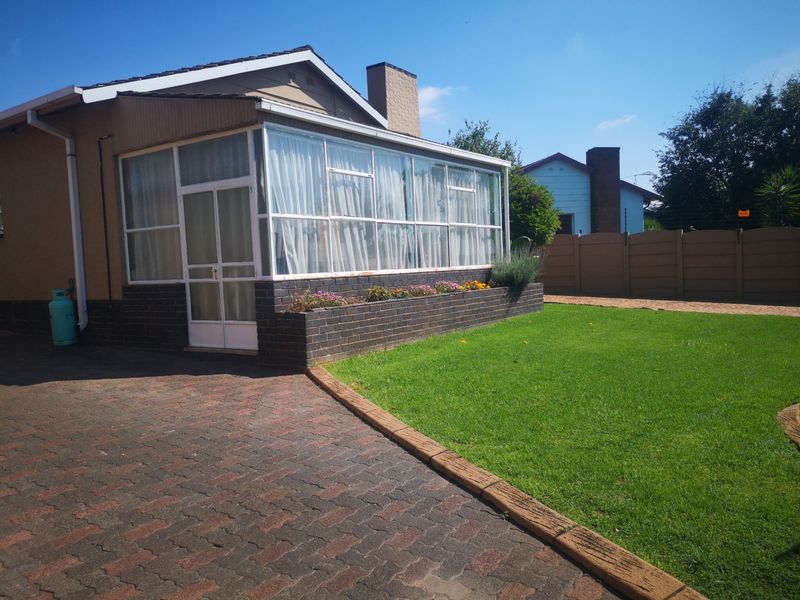 Rear view of the property featuring an enclosed patio, brick planter box, paved driveway, and a well-maintained lawn.