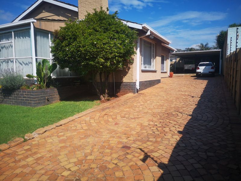 Front exterior view featuring a brick paved driveway leading to a carport, with a brick planter box and established garden area.