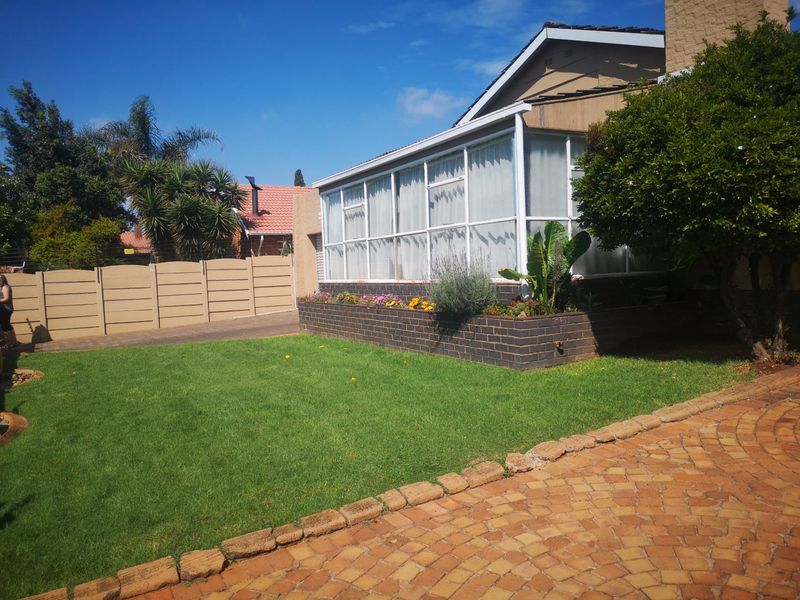 Front view of the property featuring a paved driveway, a manicured lawn, a brick planter box, and an enclosed sunroom extension.
