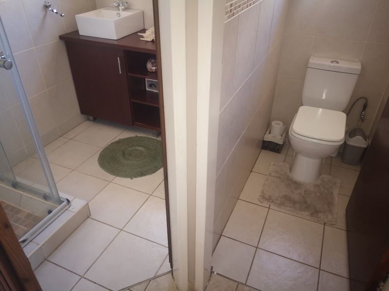 A functional bathroom featuring a separate shower enclosure, a modern vanity with a vessel sink, and a toilet with tiled finishes throughout.