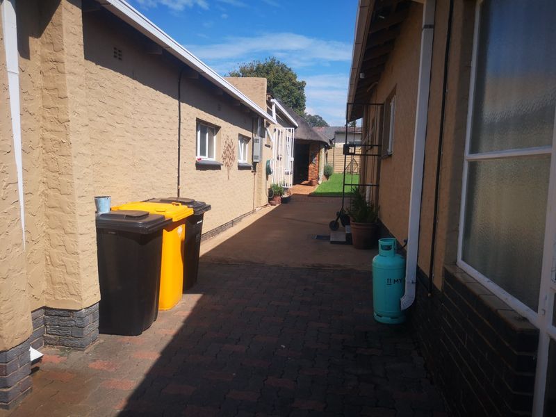 A paved side walkway between two sections of the house, featuring brick walls, downpipes, and access to the rear garden area.