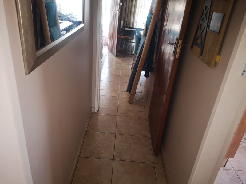 A narrow hallway featuring tiled flooring and a timber door, providing access to adjacent living spaces.