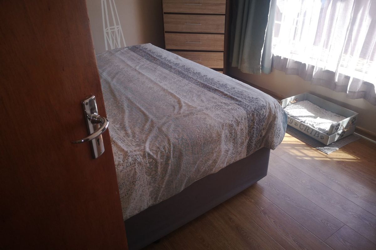 A bedroom featuring laminate flooring and a timber door, with natural light entering through the window.