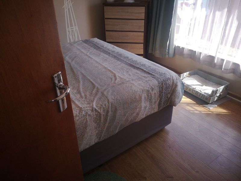 A bedroom featuring laminate flooring and a timber door, with natural light entering through the window.