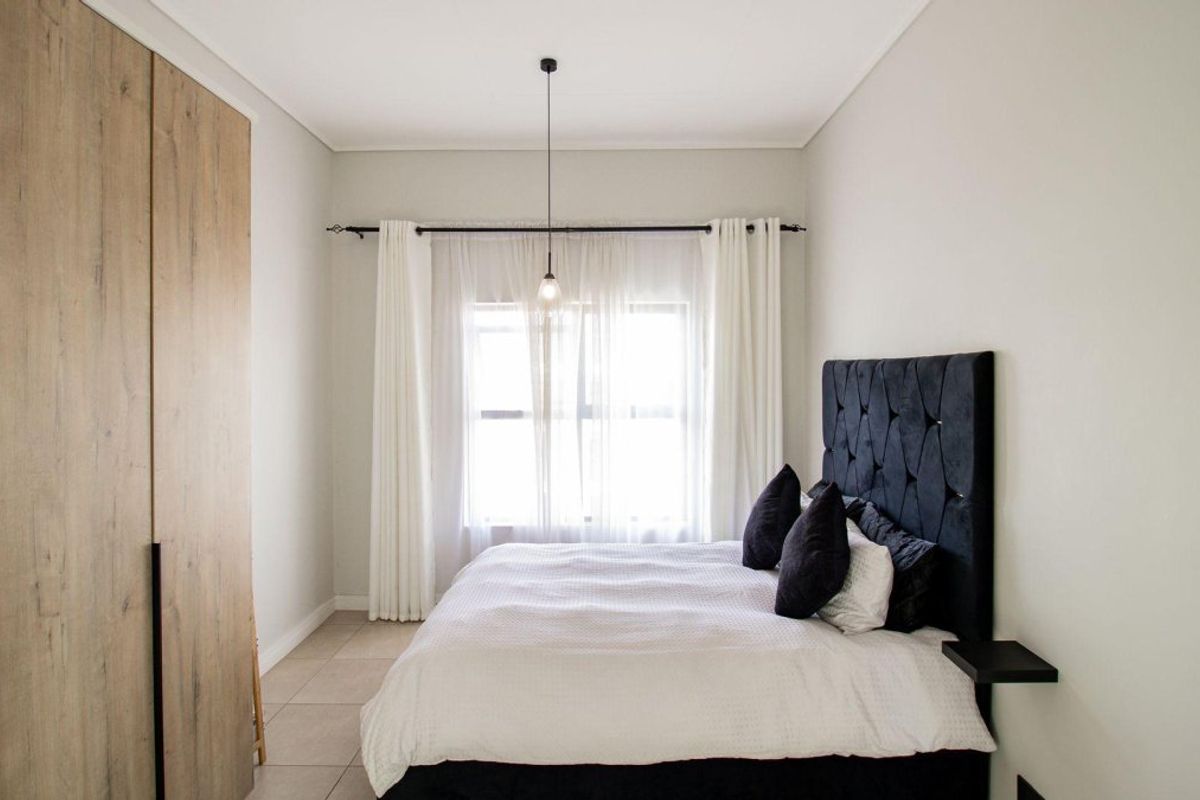 A well-maintained bedroom featuring modern built-in cupboards, neutral tiled flooring, and a minimalist pendant light fixture.