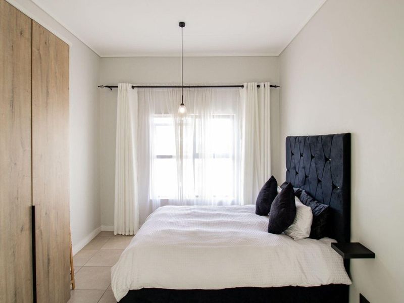 A well-maintained bedroom featuring modern built-in cupboards, neutral tiled flooring, and a minimalist pendant light fixture.