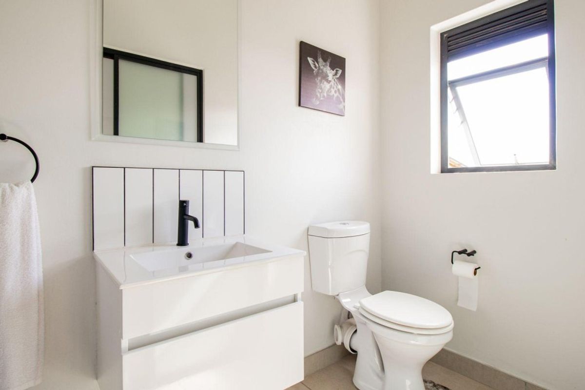 A modern, well-maintained bathroom featuring a sleek vanity with a black mixer tap, a wall-mounted mirror, and a clean white toilet.