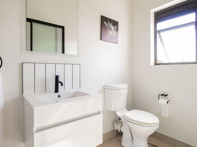 A modern, well-maintained bathroom featuring a sleek vanity with a black mixer tap, a wall-mounted mirror, and a clean white toilet.