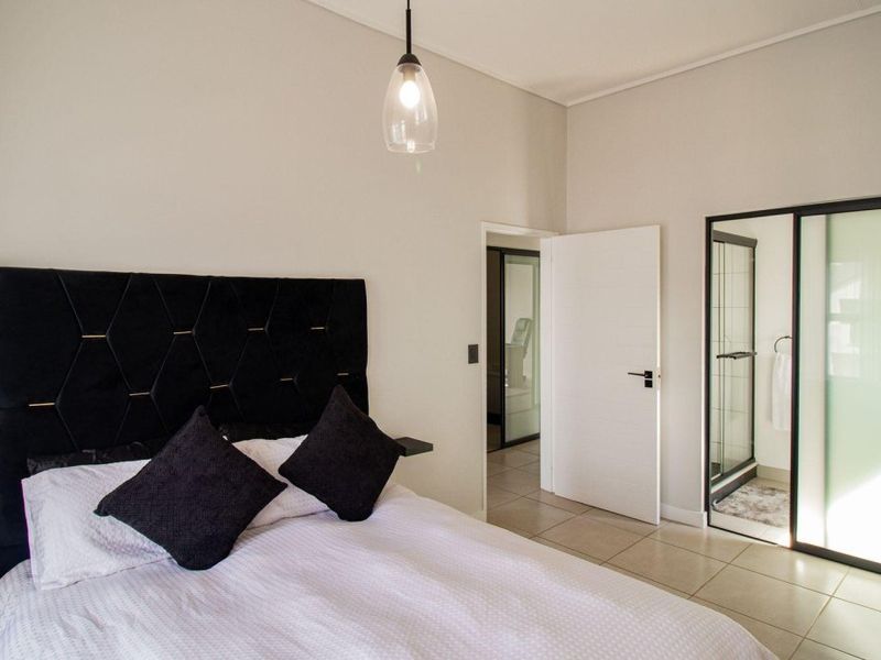 A modern bedroom featuring tiled flooring, a pendant light, and direct access to an en-suite bathroom with a glass-enclosed shower.