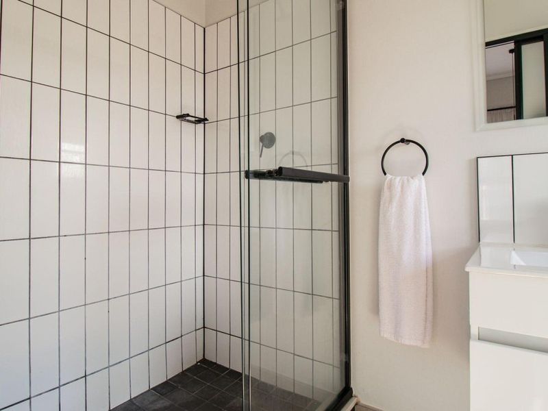 Modern bathroom featuring a walk-in shower with black-framed glass enclosure, white subway wall tiles, and a sleek vanity with a black mixer tap.