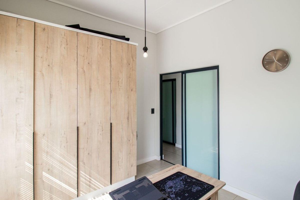 A modern bedroom featuring light wood-grain built-in wardrobes, a sleek sliding glass door, and neutral tiled flooring.