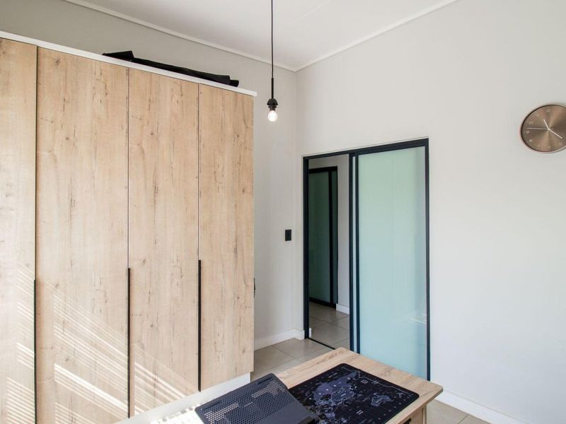 A modern bedroom featuring light wood-grain built-in wardrobes, a sleek sliding glass door, and neutral tiled flooring.