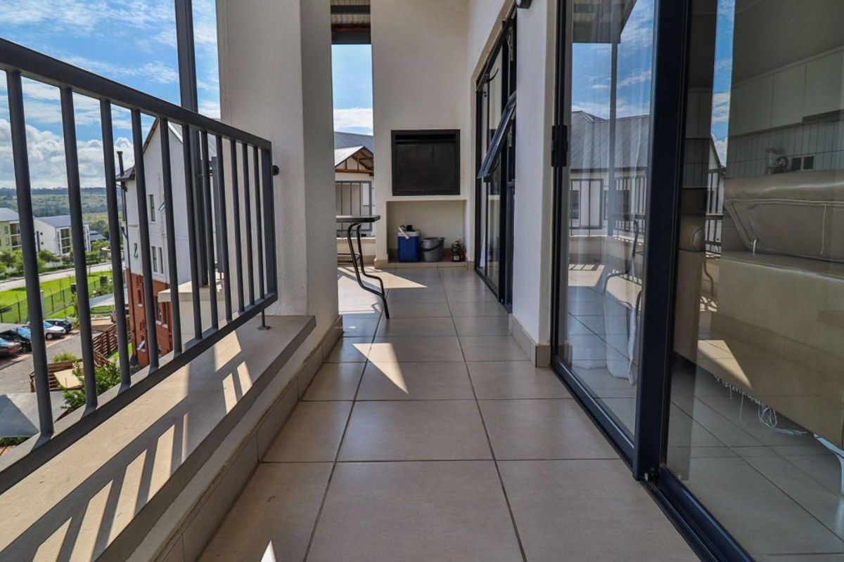 A spacious covered balcony featuring tiled flooring, a built-in braai, and metal balustrades, offering a seamless transition from the interior living area.