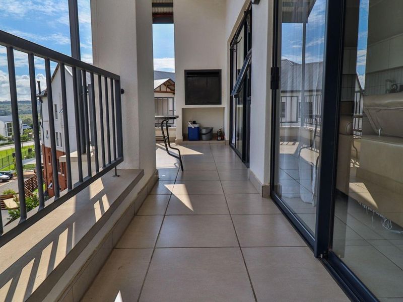 A spacious covered balcony featuring tiled flooring, a built-in braai, and metal balustrades, offering a seamless transition from the interior living area.
