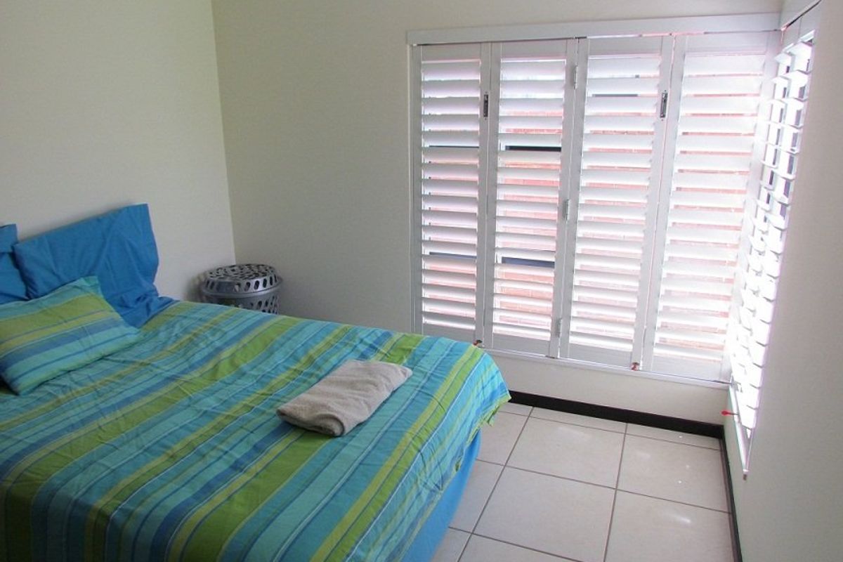 A bedroom featuring white plantation shutters and neutral ceramic floor tiles, offering a clean and functional space.