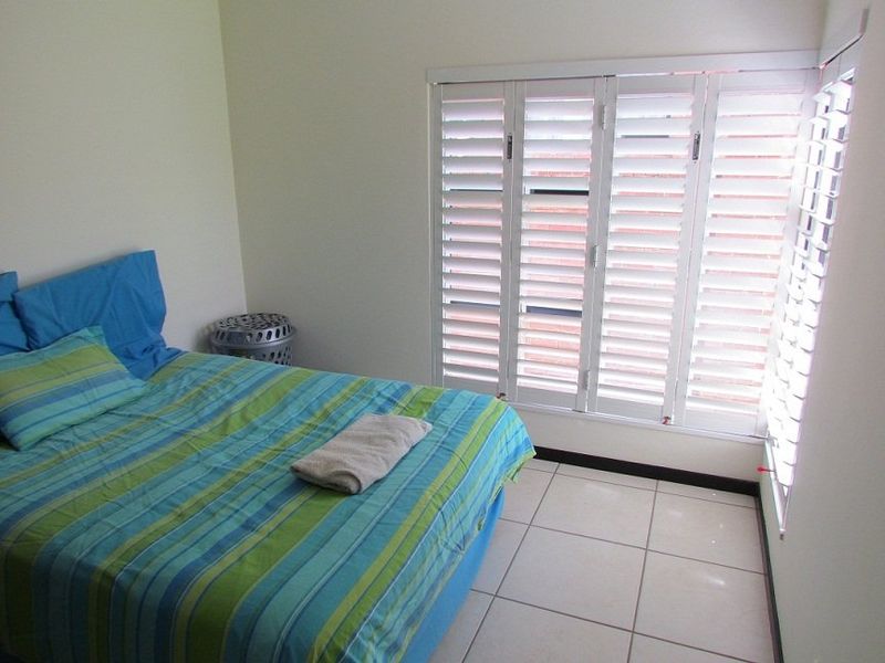 A bedroom featuring white plantation shutters and neutral ceramic floor tiles, offering a clean and functional space.