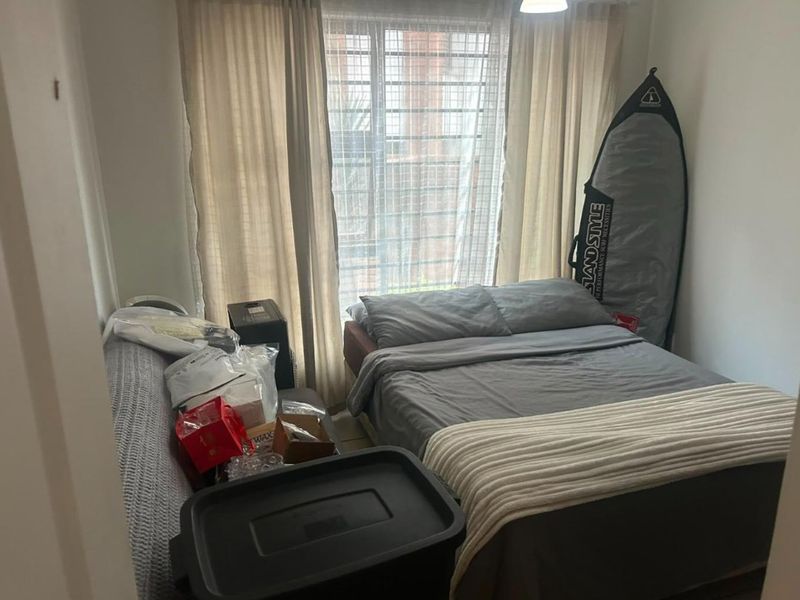 A compact bedroom featuring a window with security bars and neutral curtains, providing natural light and a functional layout.