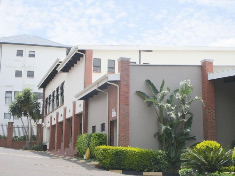 Exterior view of an apartment complex featuring a brick and rendered facade, paved driveway, and established garden landscaping.