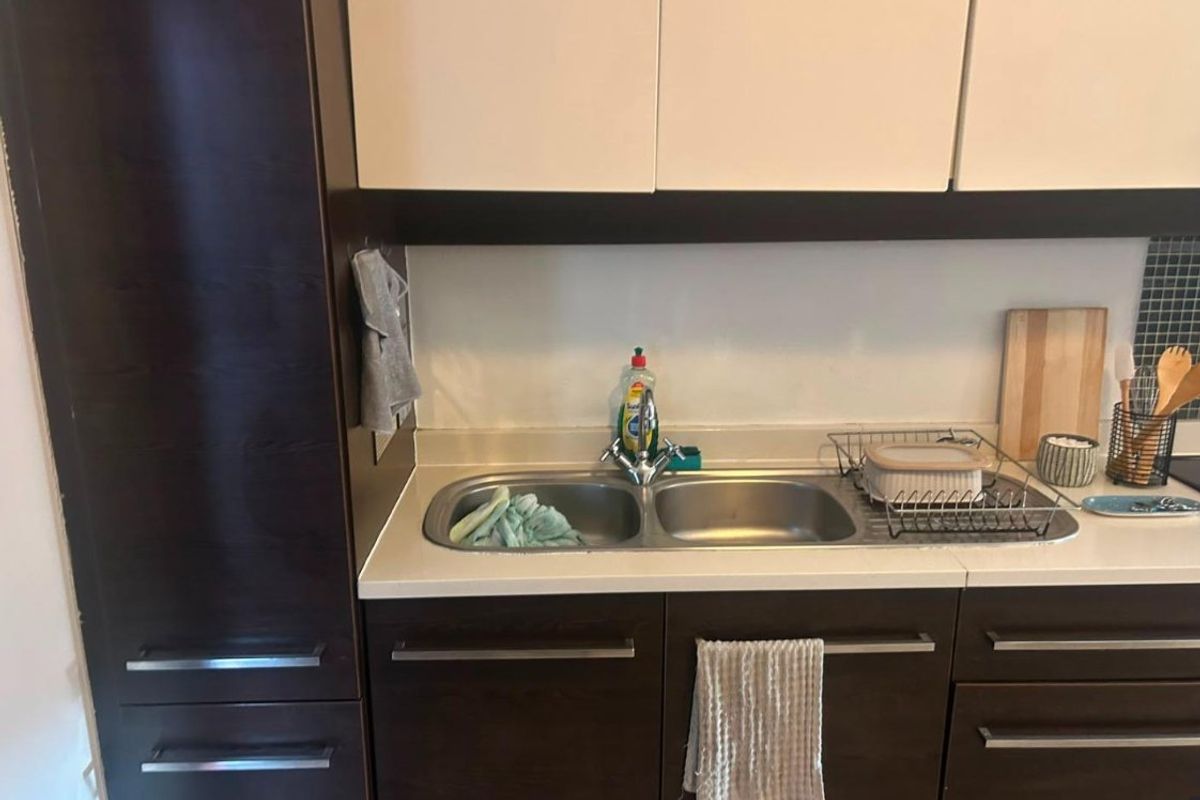 A functional kitchen area featuring dark wood cabinetry, a double bowl stainless steel sink, and a tiled backsplash.